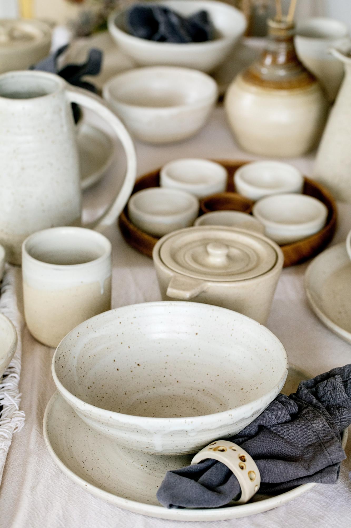 Coleção de pratos, xícaras e pires artesanais de barro dispostos lado a lado